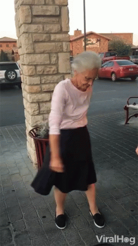 An Elderly Woman Is Dancing In Front Of A Building That Says Viral Hog GIF