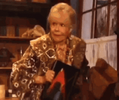 An Elderly Woman Is Holding A Book And Smiling While Sitting In Front Of A Window . GIF