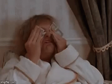 An Elderly Woman Is Laying In A Bed Covering Her Eyes With Money . GIF