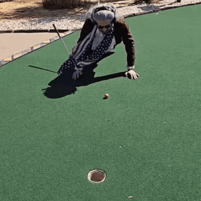 An Elderly Woman Is Playing A Game Of Golf On A Green GIF
