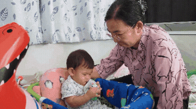 An Elderly Woman Is Playing With A Baby In A Playpen GIF