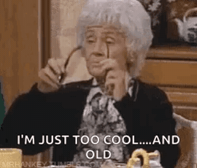 An Elderly Woman Is Sitting At A Table Holding A Pair Of Glasses . GIF