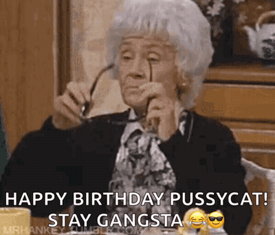 An Elderly Woman Is Sitting At A Table Holding Glasses And Saying Happy Birthday Pussycat Stay Gangsta GIF