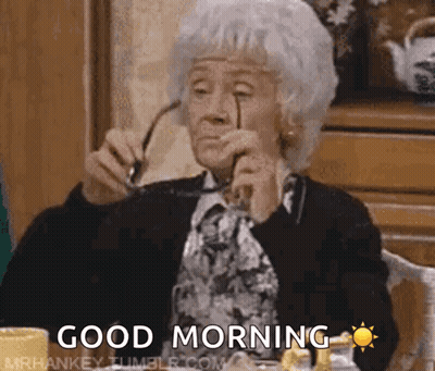 An Elderly Woman Is Sitting At A Table Holding Glasses And Says Good Morning GIF