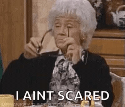 An Elderly Woman Is Sitting At A Table Holding Glasses And Says `` I Ain T Scared '' . GIF