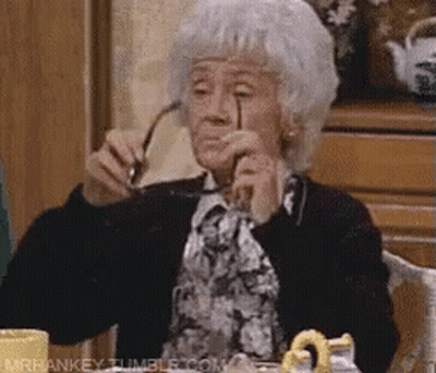 An Elderly Woman Is Sitting At A Table Holding Glasses In Her Hand . GIF