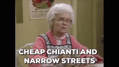 An Elderly Woman Is Sitting At A Table With A Plate Of Food And Saying `` Cheap Chianti And Narrow Streets `` . GIF