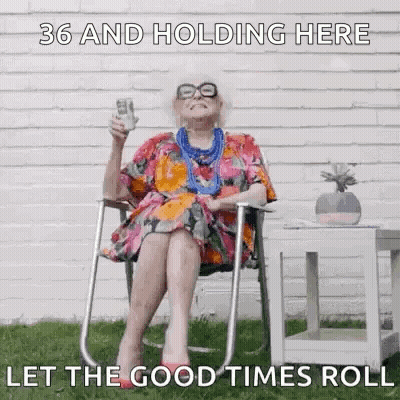 An Elderly Woman Is Sitting In A Chair Holding A Bottle Of Wine And A Dollar Bill . GIF