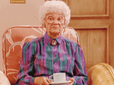 An Elderly Woman Is Sitting In A Chair Holding A Cup And Saucer GIF