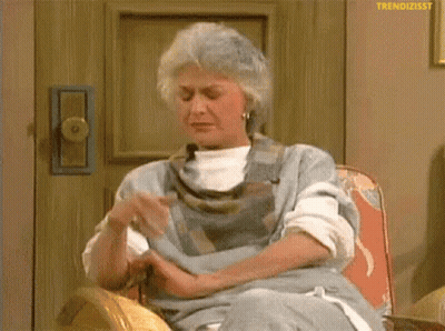 an elderly woman is sitting in a chair with her hands folded .