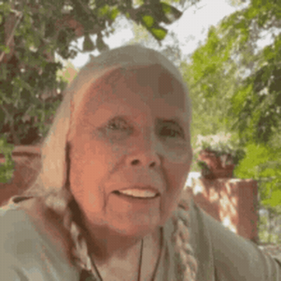 An Elderly Woman Is Smiling For The Camera While Standing In Front Of A Tree . GIF