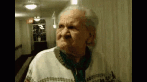 An Elderly Woman Is Standing In A Hallway And Making A Face . GIF