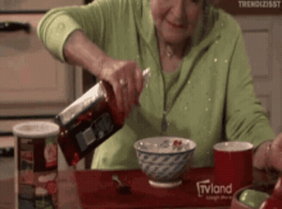 An Elderly Woman Pouring Ketchup Into A Bowl Of Cereal With A Tvland Logo On The Table GIF