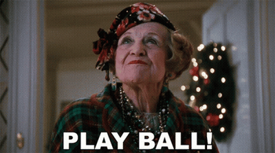 An Elderly Woman Says Play Ball In Front Of A Christmas Tree GIF