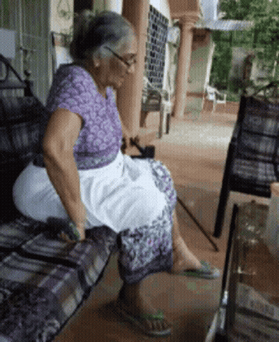 An Elderly Woman Sits On A Bench With A Cane In Her Hand GIF