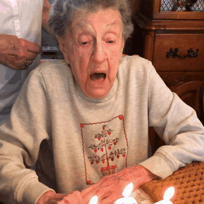An Elderly Woman Sitting At A Table With Candles In Her Hand GIF
