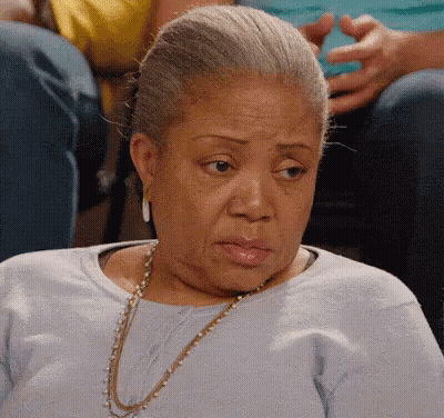 An Elderly Woman Wearing A Blue Shirt And A Gold Necklace Is Sitting In A Chair . GIF