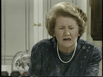 An Elderly Woman Wearing A Pearl Necklace And Earrings Makes A Funny Face GIF