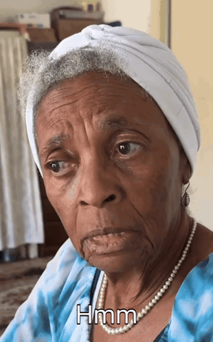 An Elderly Woman Wearing A Turban And Pearls Has The Word Hmm On Her Face GIF