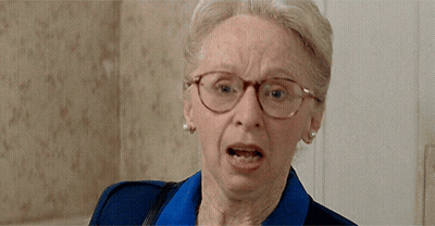 An Elderly Woman Wearing Glasses And A Blue Shirt Is Making A Funny Face GIF