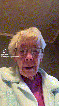 An Elderly Woman Wearing Glasses And A Pink Shirt Is Making A Funny Face While Looking At The Camera . GIF