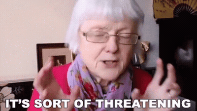 An Elderly Woman Wearing Glasses And A Scarf Is Making A Threatening Gesture . GIF
