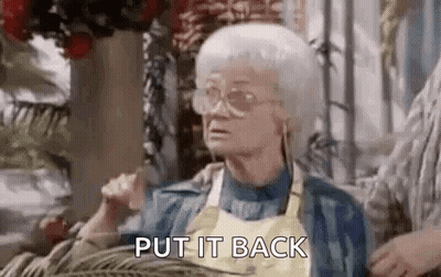 An Elderly Woman Wearing Glasses And A Yellow Apron Is Sitting On A Couch And Saying `` Put It Back '' . GIF