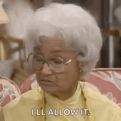 An Elderly Woman Wearing Glasses And A Yellow Shirt Is Sitting On A Couch And Saying `` I 'Ll Allow It '' GIF