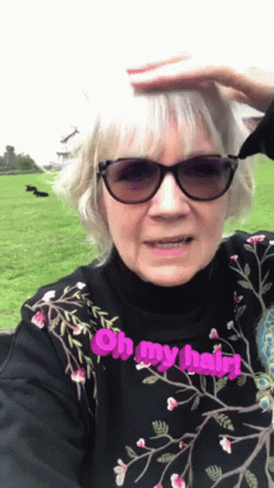 An Elderly Woman Wearing Sunglasses And A Black Shirt Says Oh My Hair GIF