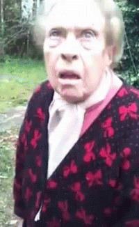 An Elderly Woman With A Surprised Look On Her Face Is Wearing A Red And Black Cardigan GIF