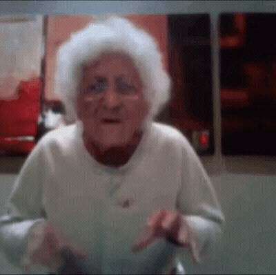 An Elderly Woman With Gray Hair Is Standing In Front Of A Wall . GIF