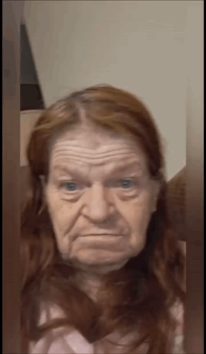 An Elderly Woman With Red Hair Is Making A Funny Face And Looking At The Camera . GIF