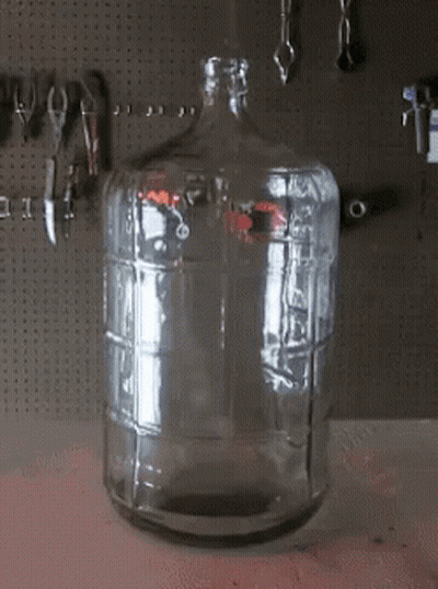 An Empty Glass Bottle Sits On A Table In Front Of Tools GIF