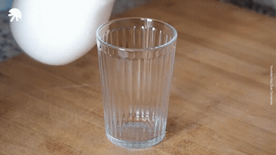 An Empty Glass Sits On A Wooden Table With A White Arrow Pointing Up GIF