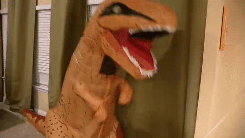 An Inflatable T-Rex Is Standing In Front Of A Window With Its Mouth Open GIF
