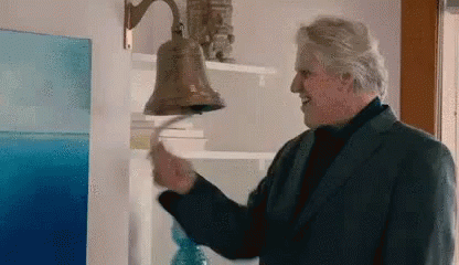 An Older Man In A Suit Is Ringing A Bell On A Wall . GIF