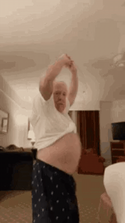 An Older Man Is Dancing In A Living Room While Holding His Arms Up . GIF
