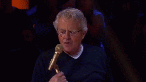 An Older Man Is Holding A Microphone And Talking Into It . GIF