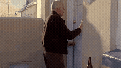 An Older Man Is Knocking On A Door With A Bottle Of Beer In Front Of Him . GIF