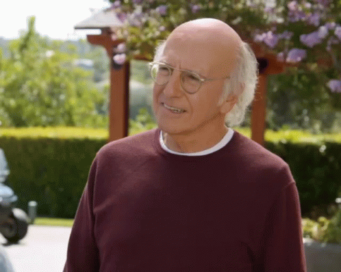 An Older Man Wearing Glasses And A Maroon Sweater Is Smiling GIF