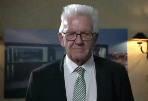 An Older Man Wearing Glasses And A Suit Is Looking At The Camera GIF