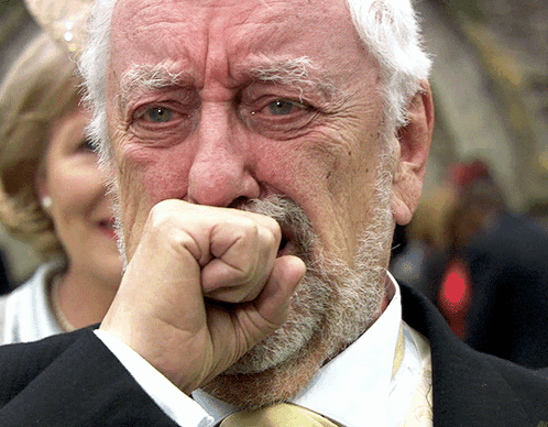 An Older Man With A Beard Covering His Mouth With His Fist GIF