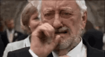 An Older Man With A Beard Is Crying And Covering His Mouth With His Hand . GIF