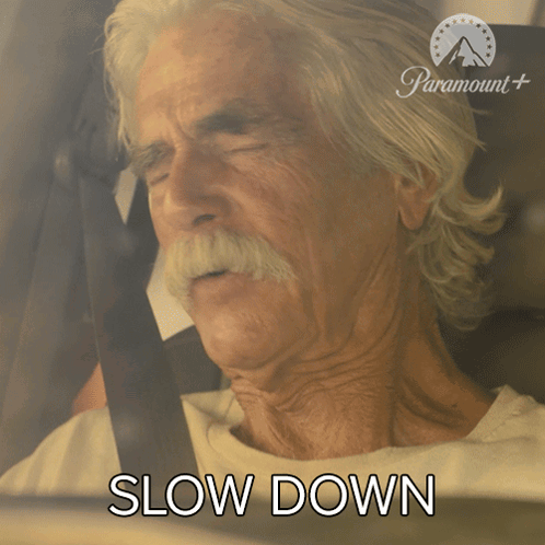 An Older Man With A Mustache Is Sitting In A Car With The Words Slow Down Behind Him GIF