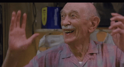 An Older Man With A Mustache Is Smiling And Waving His Hands In A Kitchen . GIF