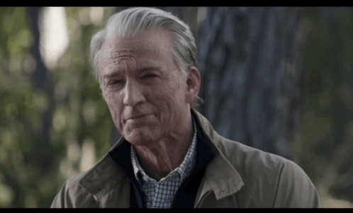 An Older Man With Gray Hair Is Wearing A Tan Jacket And A Plaid Shirt GIF