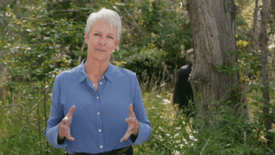 An Older Woman In A Blue Shirt Is Standing In The Woods GIF