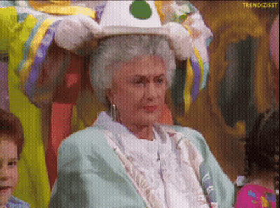An Older Woman Is Wearing A Clown Costume And Holding A Hat On Her Head GIF