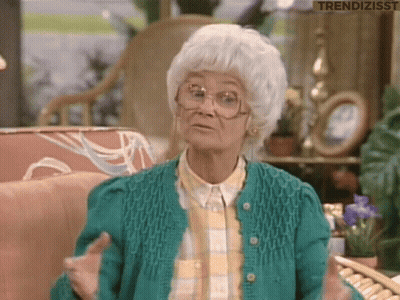 An Older Woman Wearing Glasses And A Green Sweater Is Sitting In A Living Room . GIF