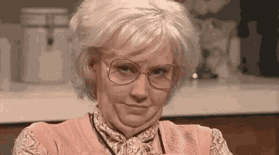 An Older Woman Wearing Glasses And A Pink Shirt Is Making A Funny Face . GIF